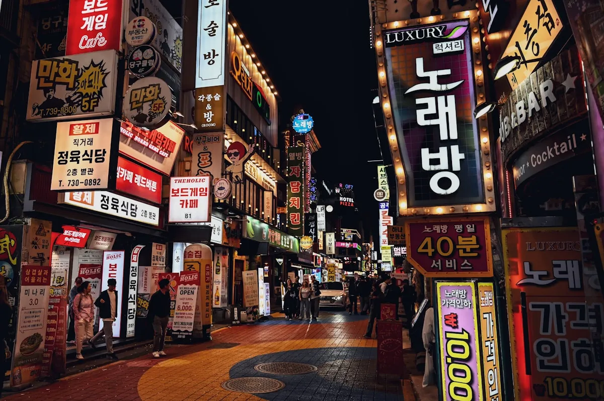 Neon-lit Seoul nightlife street packed with glowing Korean signs for karaoke rooms, restaurants, and shops