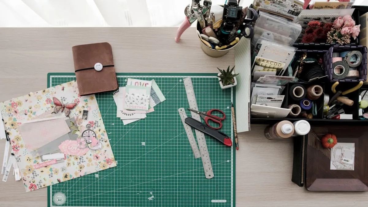 Overhead view of a craft seller's workspace — green cutting mat, scrapbooking papers, ribbons, scissors, and bins of supplies