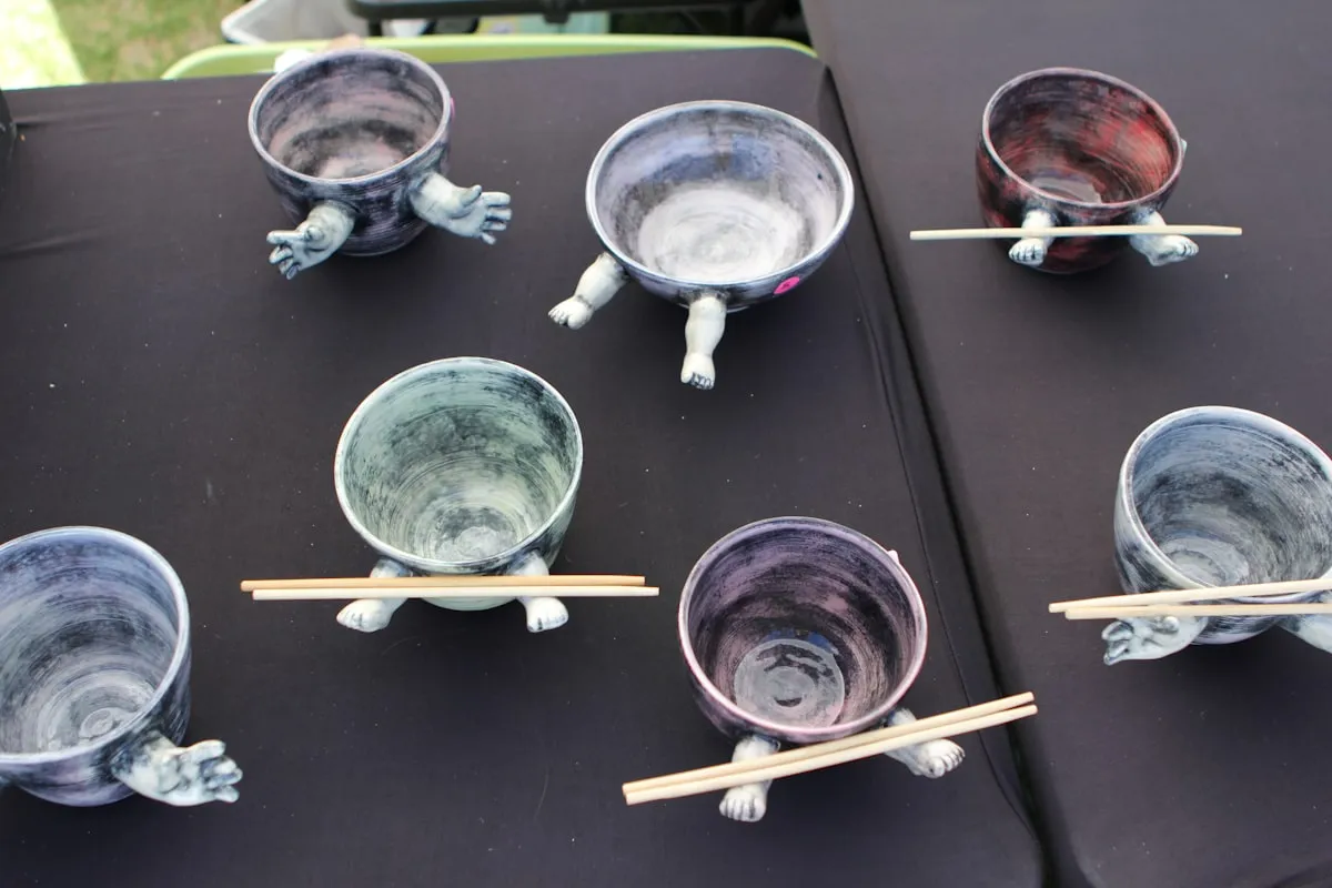 Handmade ceramic turtle-shaped bowls with chopsticks displayed on a black-cloth craft fair table