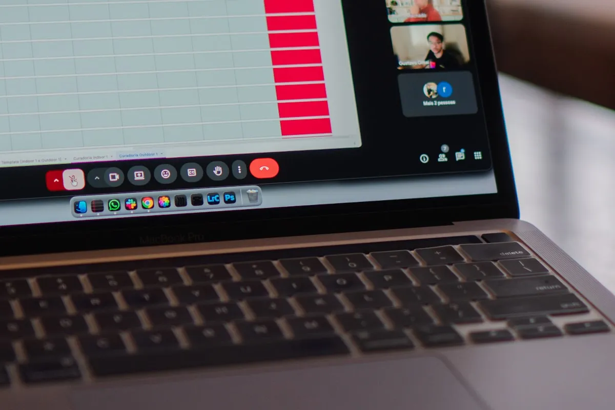 Close-up of a MacBook Pro screen showing a spreadsheet template with rows of empty cells and red status bars next to an open video meeting panel