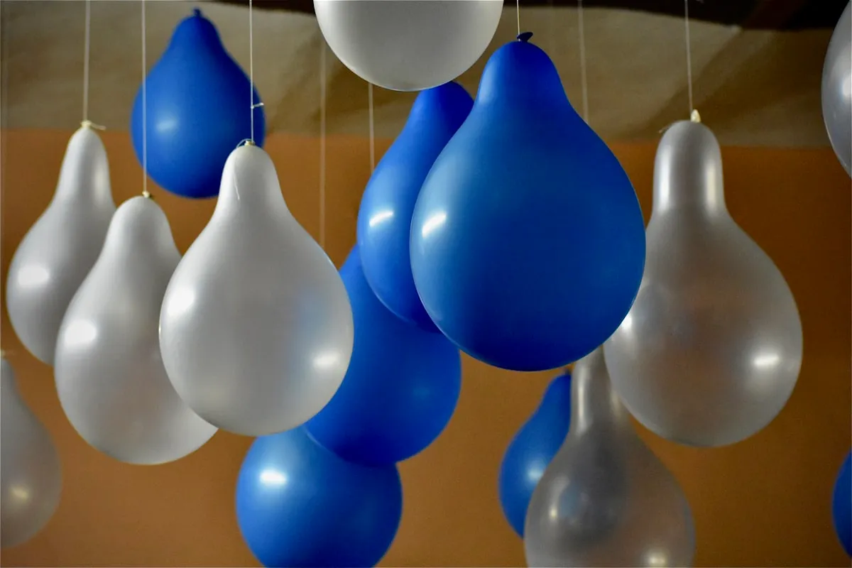 Cluster of blue, white, and silver helium balloons hanging from strings as overhead party decor at a baby shower