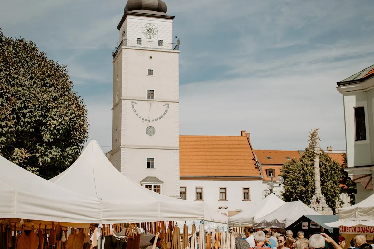 Rows of white canopy stalls set up across a sunlit town square at an outdoor craft market, with handmade wooden goods displayed at the front booth