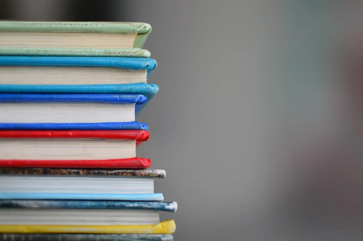 Close-up of a tall stack of hardcover books with green, blue, red, and yellow spines against a soft grey background
