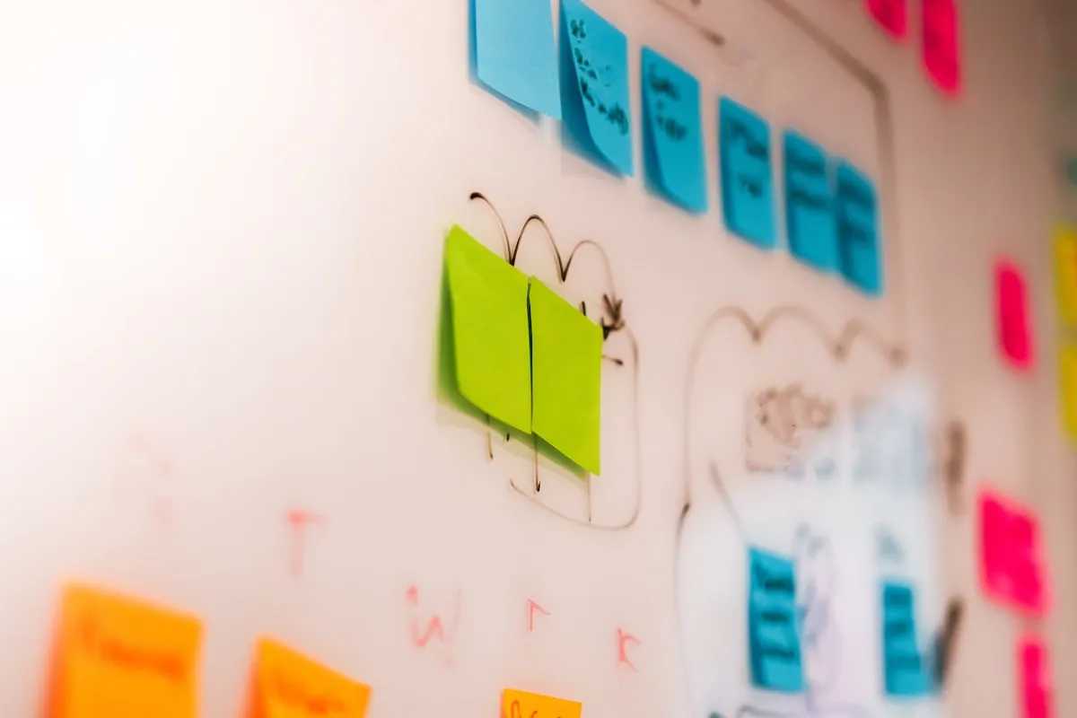 Close-up of a kanban whiteboard covered in blue, green, orange, and pink sticky notes arranged into workflow columns