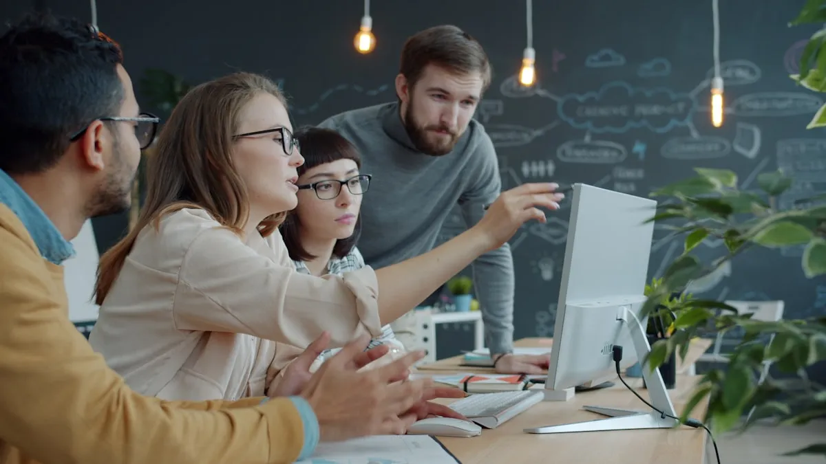 Young professionals collaborating around a computer monitor in a modern office, discussing a project together