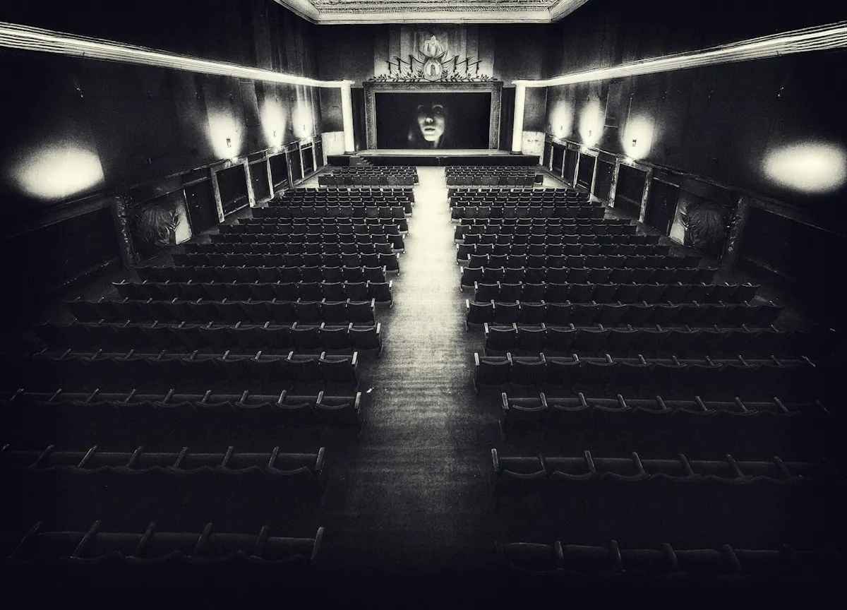 Black-and-white vintage cinema hall with empty rows of seats facing a large screen showing a film, ready for a summer movie crowd