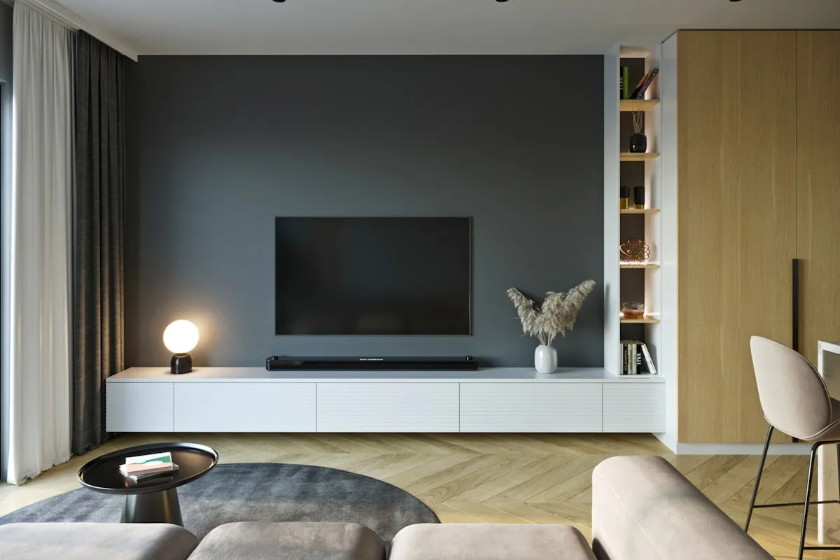 A modern minimalist living room with a dark feature wall, wall-mounted television, low white console, soundbar, and a soft beige sectional couch — the quiet stage where most watchlists go to live and never get watched