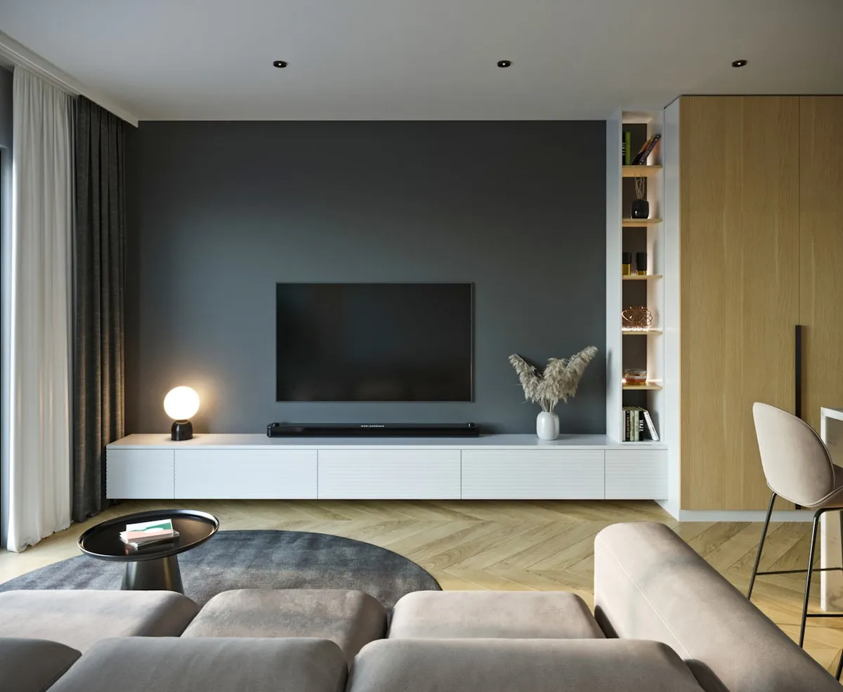A dim, minimalist living room with a wall-mounted television facing a soft grey couch — the quiet stage where most watchlists go to live and never get watched