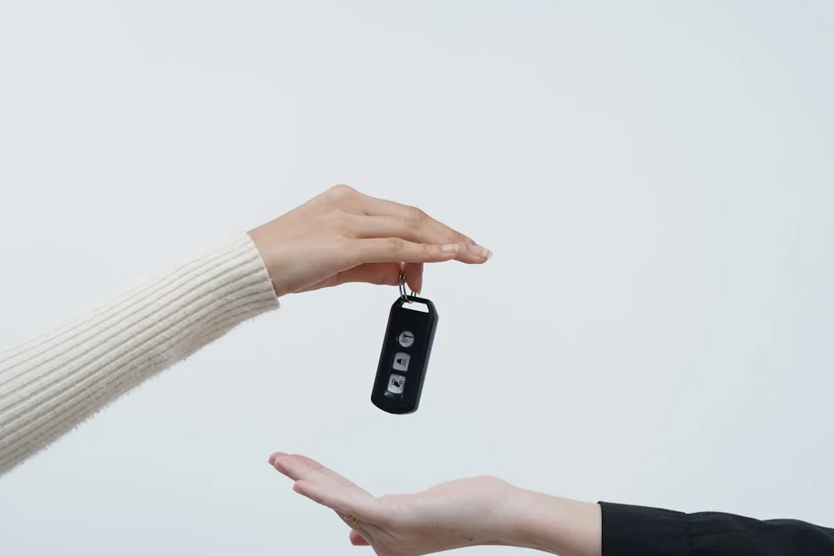 Hand passing a black car key fob to an outstretched palm against a clean grey background — the brief moment that hides most of the markup that came before it