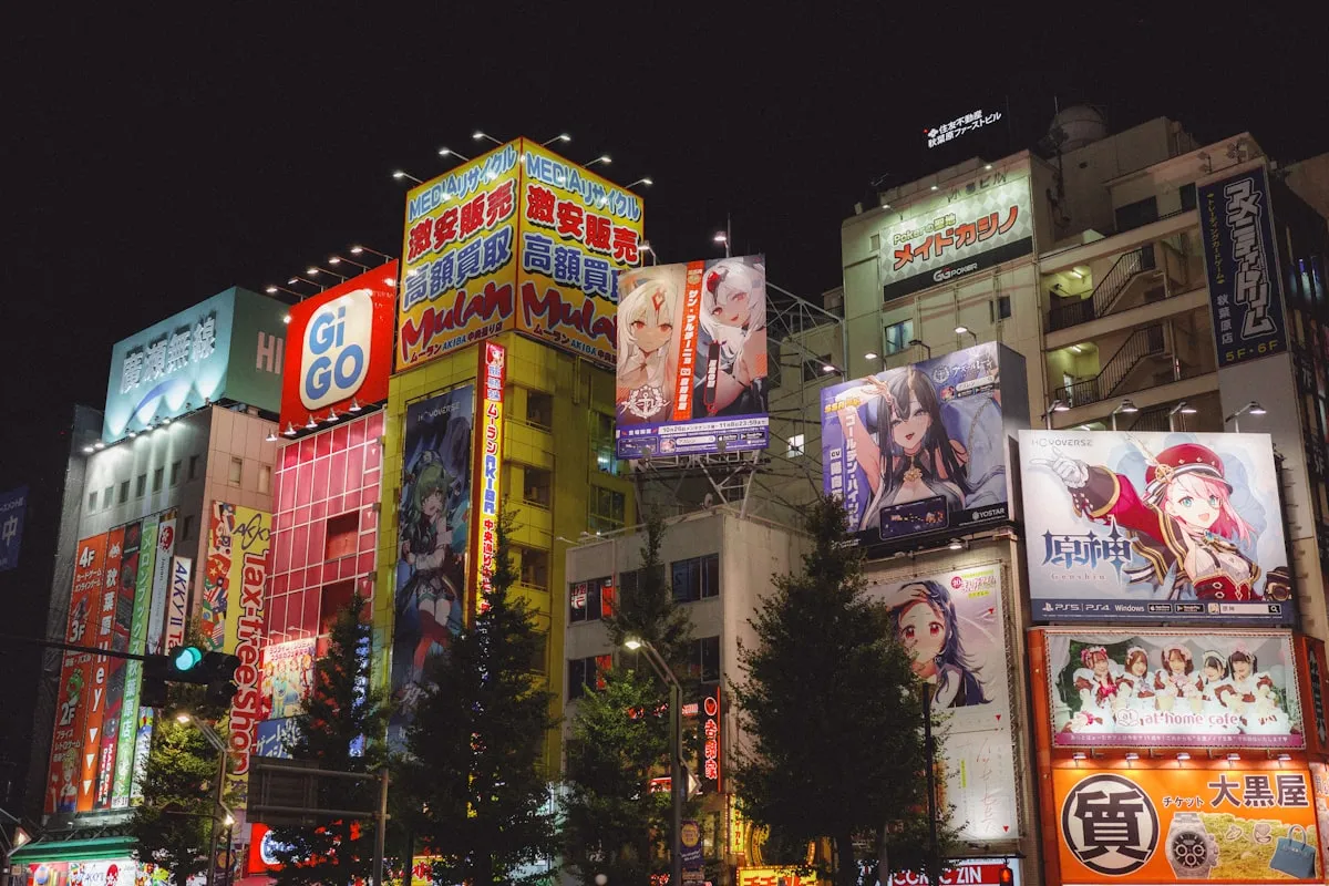 Akihabara at night with brightly lit anime billboards, manga and game store signs, and Japanese-text neon stacked across the buildings