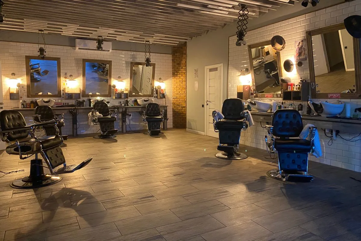 Rows of empty black barber chairs facing wood-framed mirrors in a dimly lit barbershop