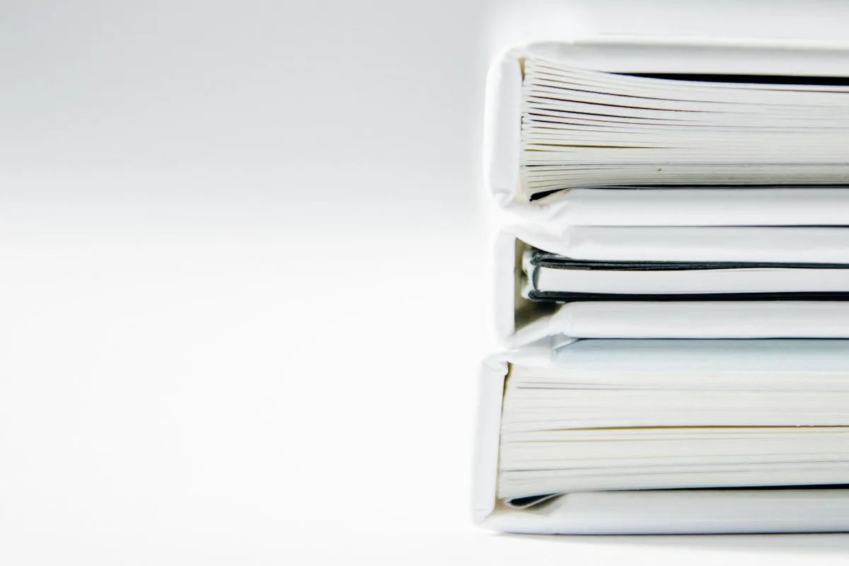 A close-up side view of a neat stack of three thick white ring binders on a plain white background.