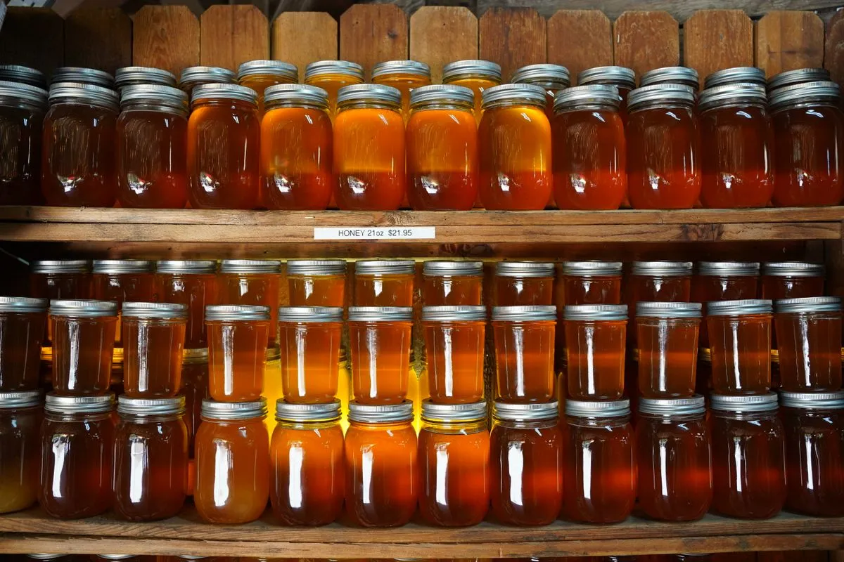 Two wooden shelves of honey in mason jars, from pale gold to deep amber, with a shelf tag reading Honey 21oz