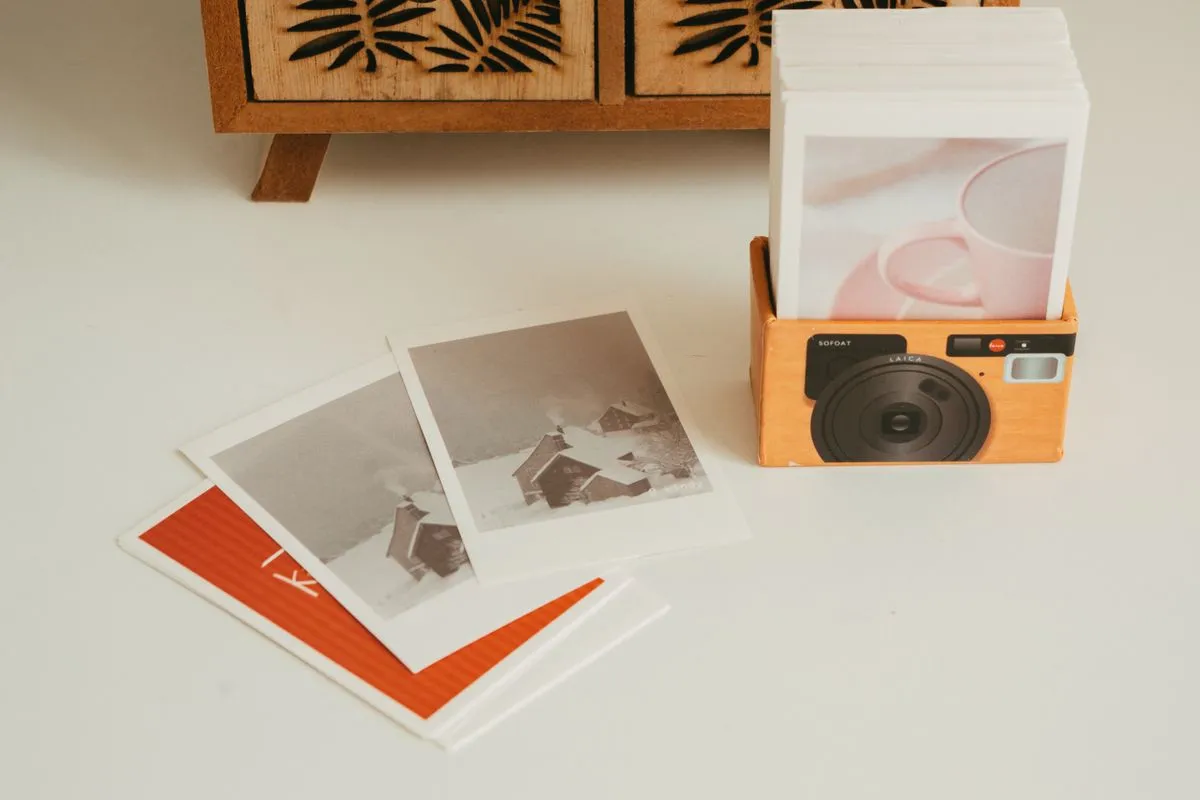 Instant-style photo prints standing in an orange camera-shaped holder, with loose prints fanned out on a white table
