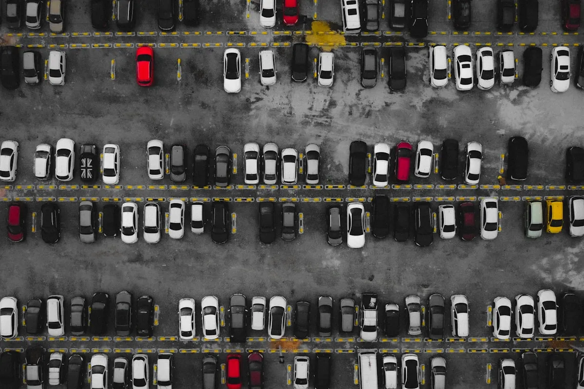 Aerial view of a packed parking lot, with rows of white, black and red cars filling nearly every marked space between yellow-striped lanes