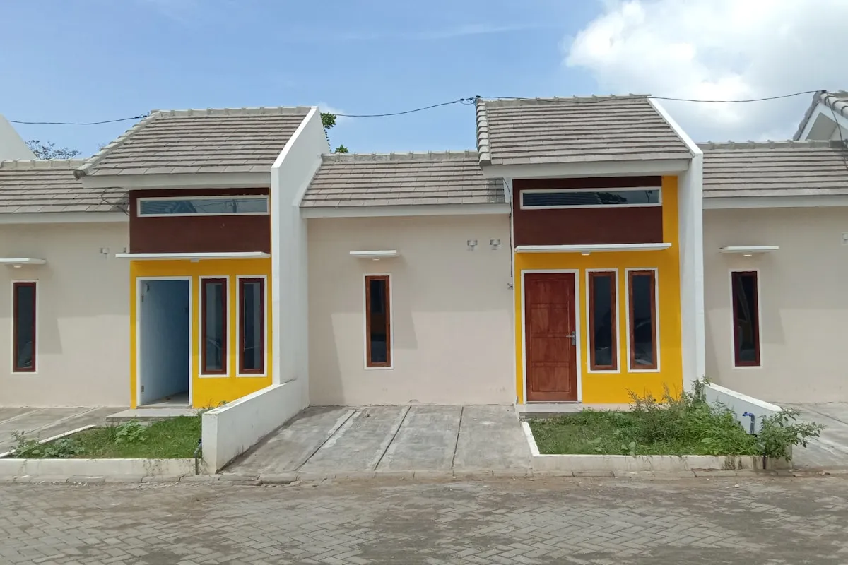 Two adjoining single-story rental units with pale stucco walls, tiled roofs and bright yellow door surrounds, photographed from the empty paved street in front