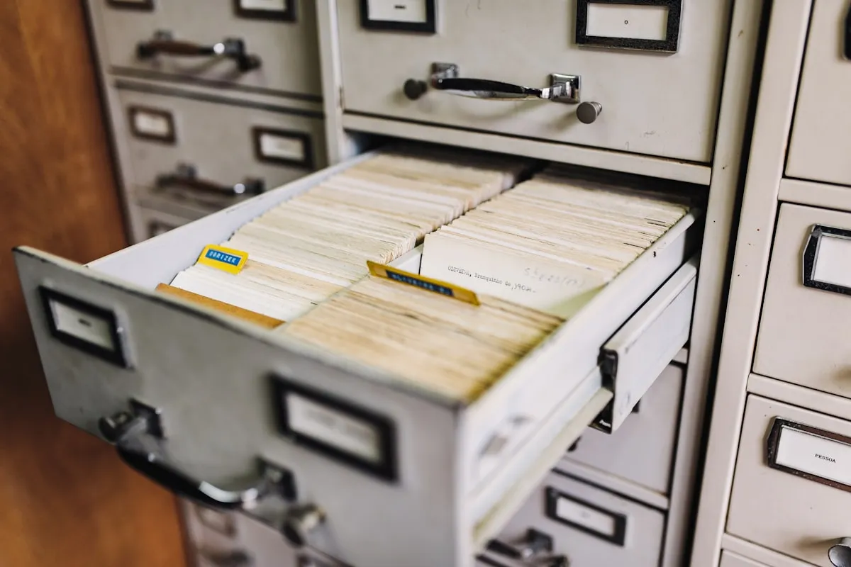 An open metal card-index drawer pulled out from a wall of pale filing cabinets, packed tight with rows of aged paper record cards and colored divider tabs